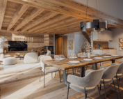 Perspective 3D intérieure d'un chalet de luxe avec salon en vieux bois, grande cheminée centrale et vue sur les sommets enneigés, projet Le Chalet de Glace.